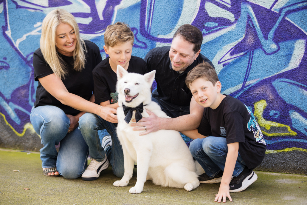 Family portraits gathered around their white husky leaning on an art mural in downtown Santa Ana.