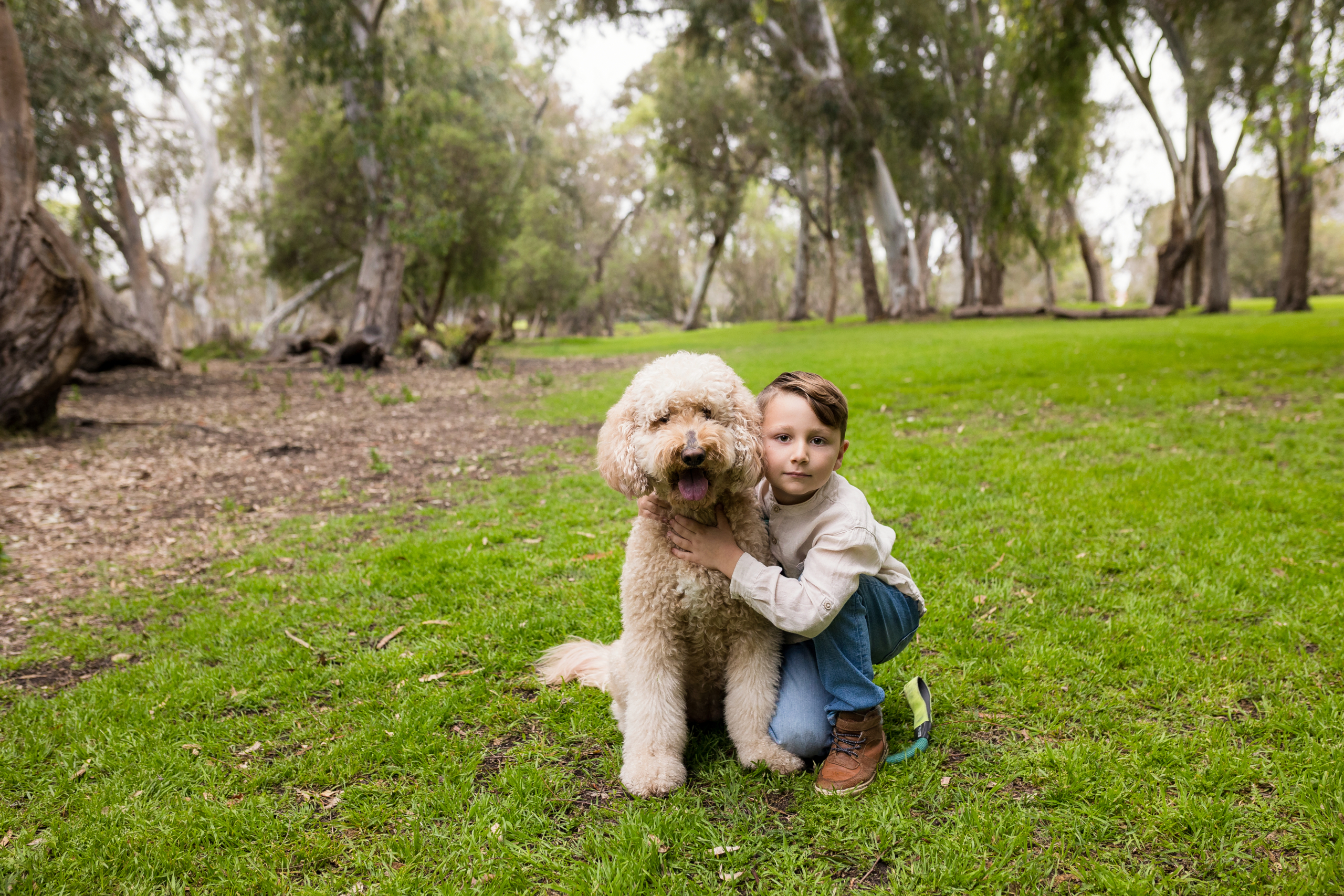 Picture of a 7 year old boy with his family pet dog wearing jeans and a cream shirt posing at Huntington Beach Central Park.