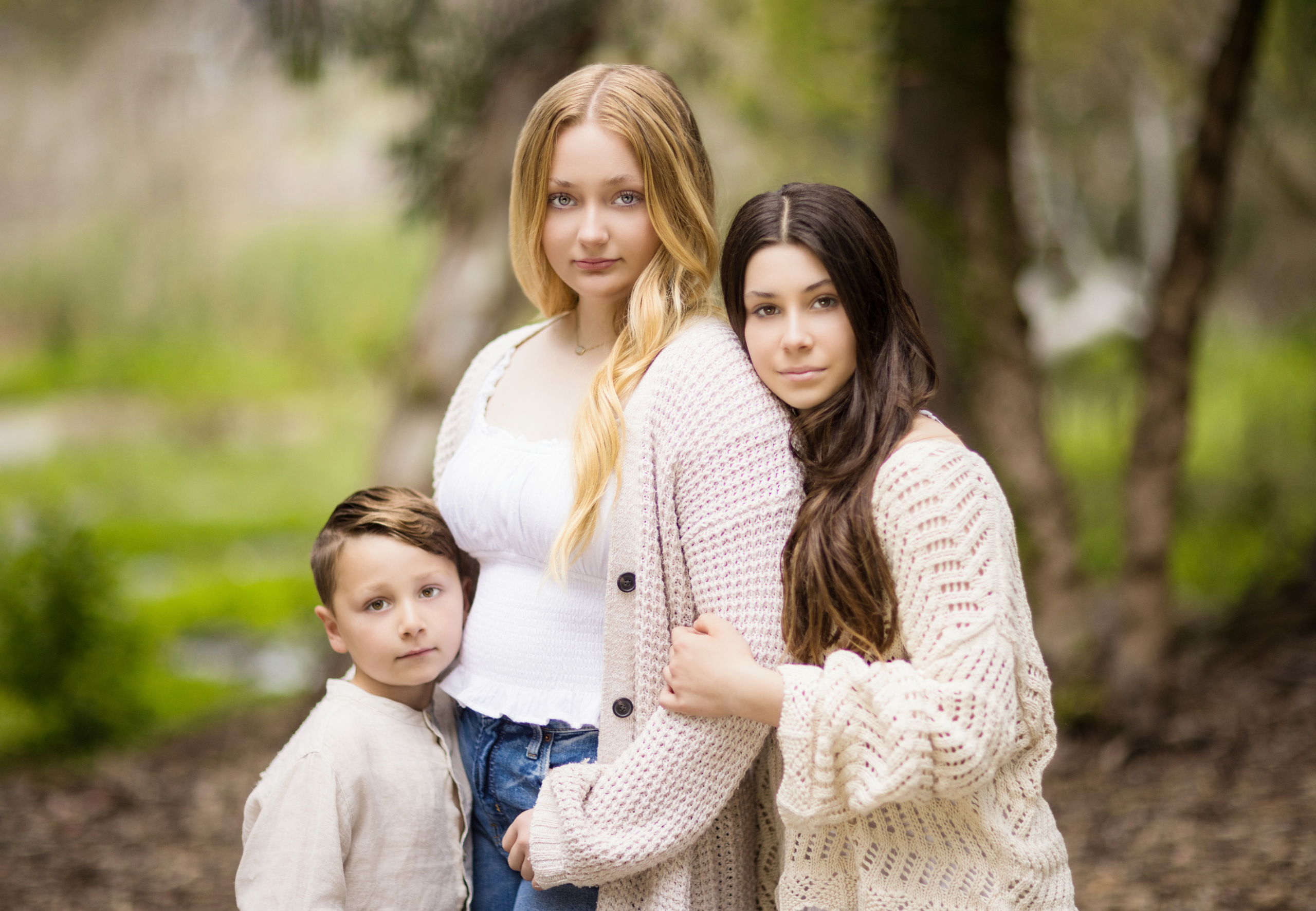 Brother and two sisters wearing white and cream with jeans posing for a family portrait in Huntington Beach Central Park on a cloudy day.