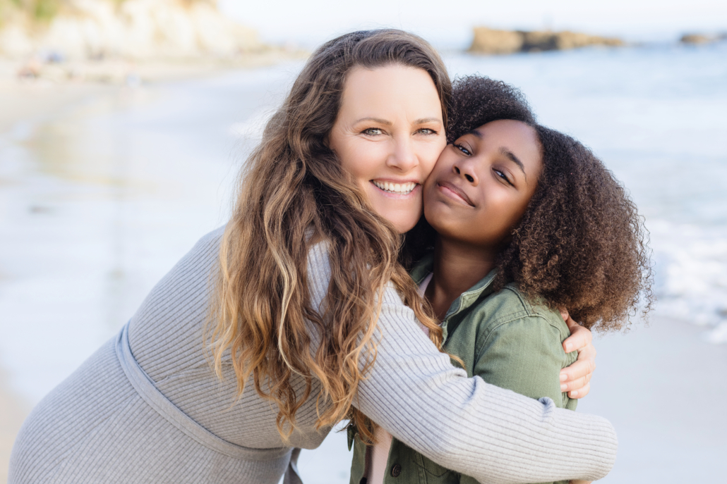 A close-up shot of mother and daughter sharing a joyful embrace, their faces illuminated by the golden hour light at Laguna Beach.