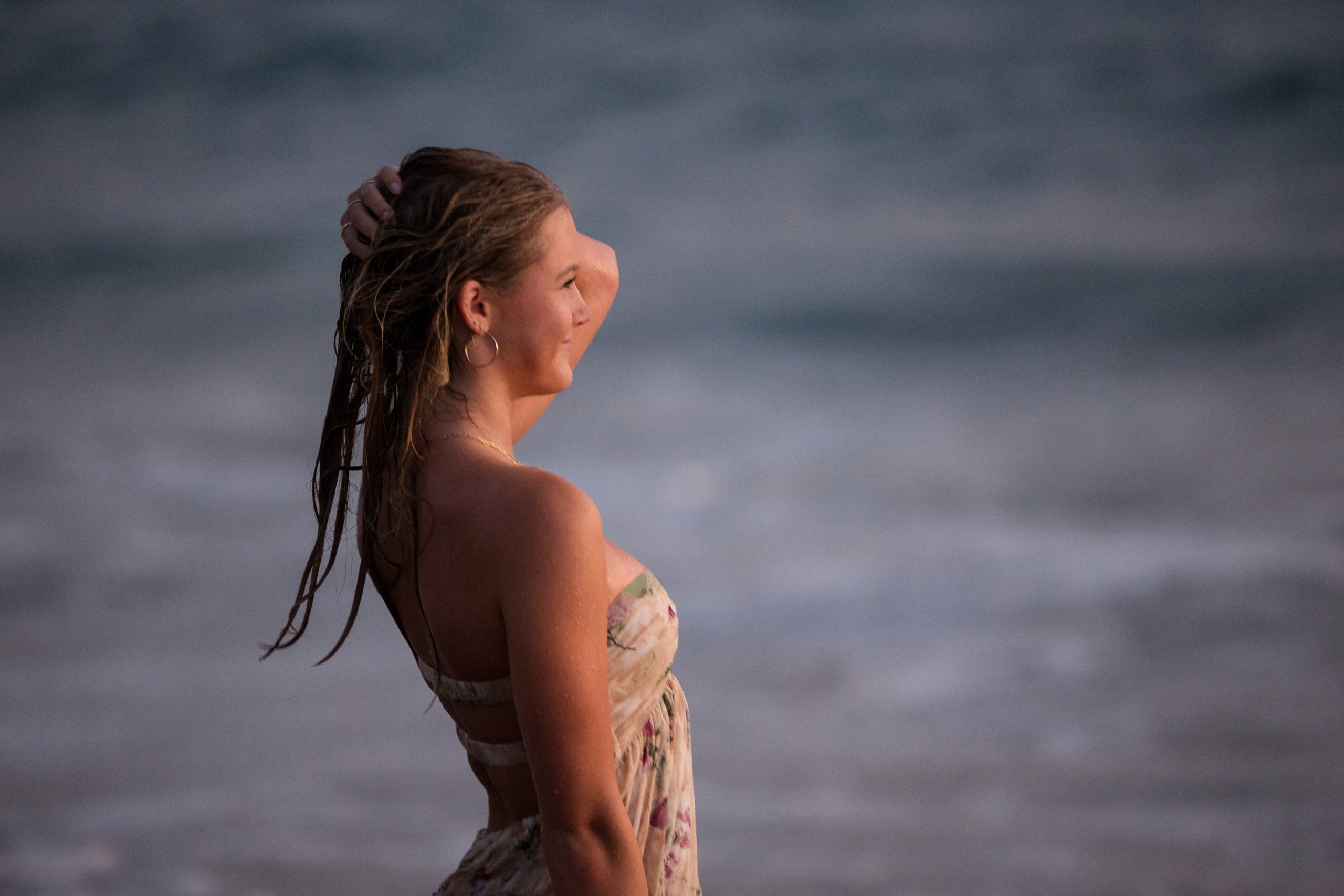 A candid close-up of a young woman with wet hair, standing against the blurred backdrop of the ocean, exuding confidence and serenity.